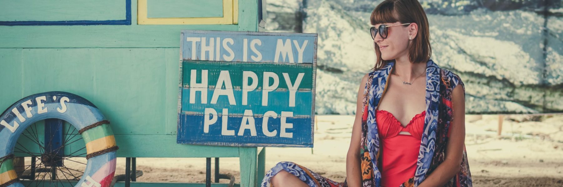 woman sitting next to happy place sign